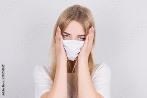 Sick girl in a protective medical mask holds her temples with her hands because of the high temperature. Illness, coronavirus and seasonal cold concept.