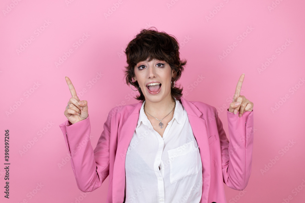 Young business woman over isolated pink background amazed and surprised looking at the camera and pointing up with fingers and raised arms Young business woman over isolated pink background amazed and surprised looking at the camera and pointing up with fingers and raised arms