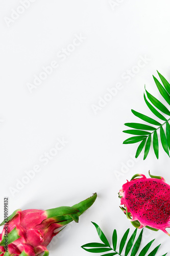 Fresh organic pink dragon fruit, pitaya or pitahaya, on white background with copy-space. Trendy top view of this exotic fruit cut in half with palm leaves.