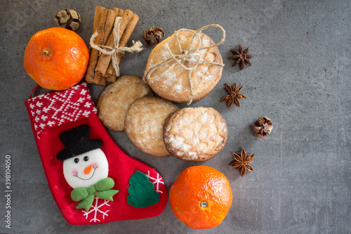 Christmas stocking, cinnamon sticks, tangerines and cookies on dark gray background with copy space. Festive decorations top view photo.  