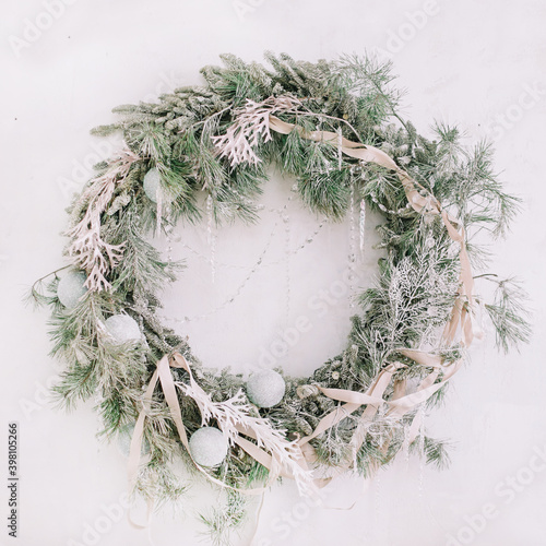 Christmas wreath with fir branches and decorations hanging on white wall. Merry Christmas. Festive holiday decoration.