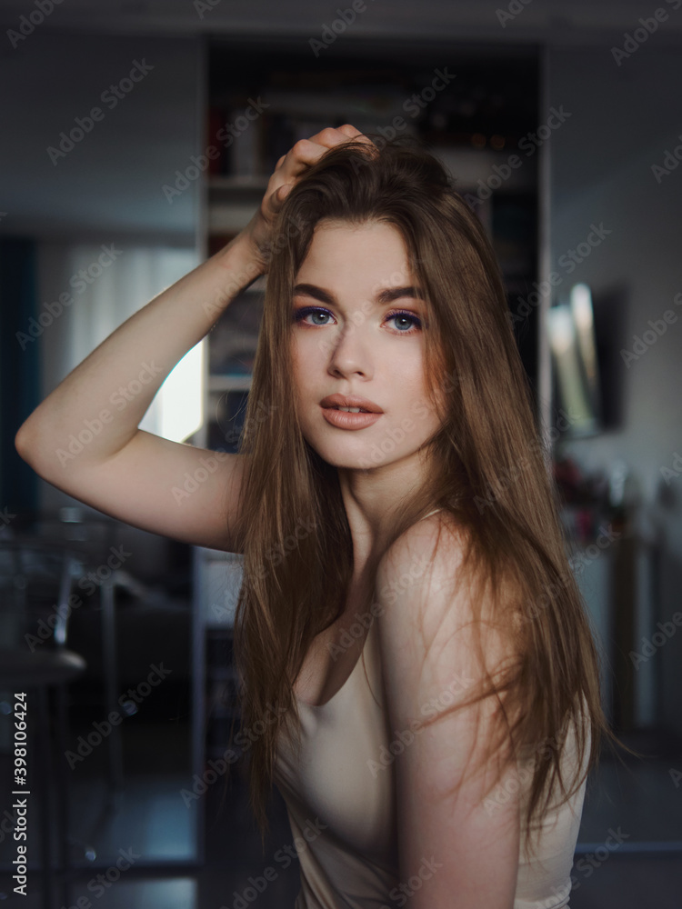 Fototapeta premium Fashion photo of beautiful young beautiful woman with gorgeous natural lips wearing shoulder straps blouse relaxing and smiling in dark room staring into camera