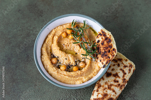 Classic hummus with rosemary, flatbread, boiled chickpea and olive oil, green stone background. Traditional Middle Eastern snack. Top view.