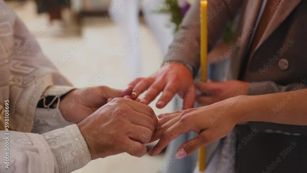 A caucasian priest in a white special chasuble performs the wedding ceremony and reads a prayer and puts wedding rings on the newlyweds standing in the church opposite him and holding tall wax candles A caucasian priest in a white special chasuble performs the wedding ceremony and reads a prayer and puts wedding rings on the newlyweds standing in the church opposite him and holding tall wax candles