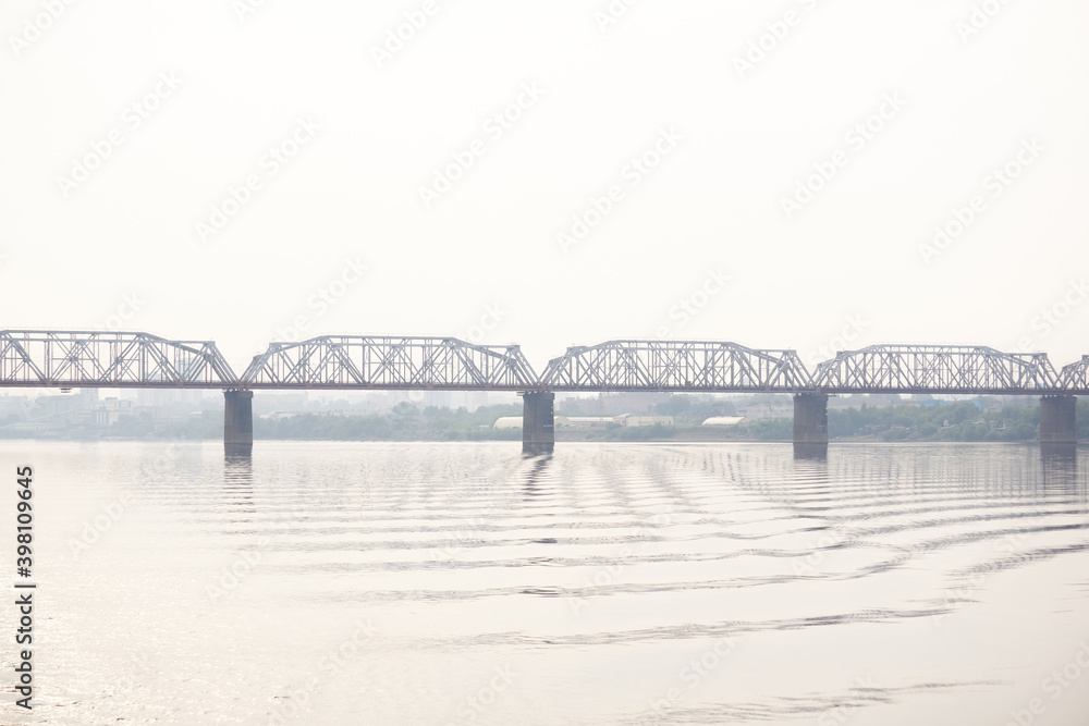 Obraz premium railroad bridge over a wide river and the silhouette of a distant city behind it in the morning fog