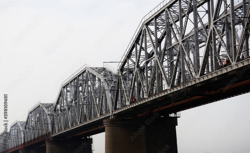 several spans of a railway truss bridge against a cloudy sky