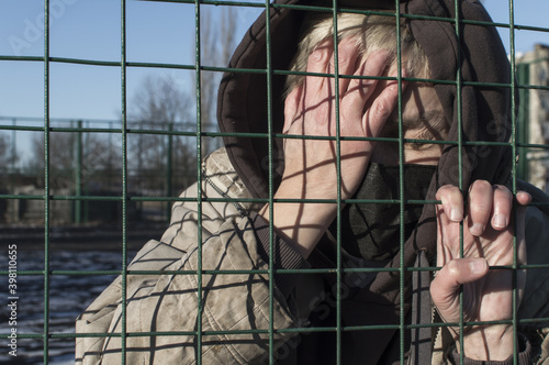 Homeless. A woman in dirty ragged clothes and a medical mask holds on to the bars and cries.