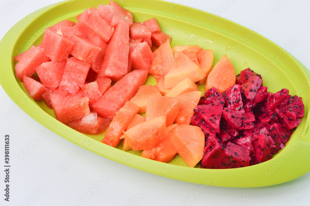 Side view of watermelons, papayas and dragon fruits assortment on a green plate.  Tropical fruits on a white background.