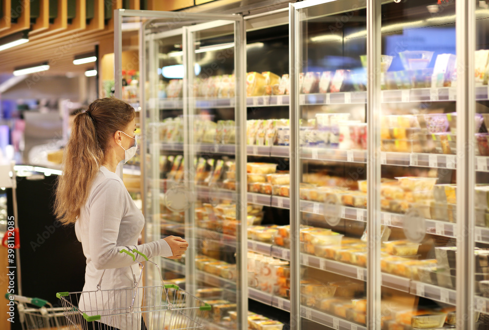 Woman choosing frozen food from a supermarket freeze.Supermarket shopping, face mask