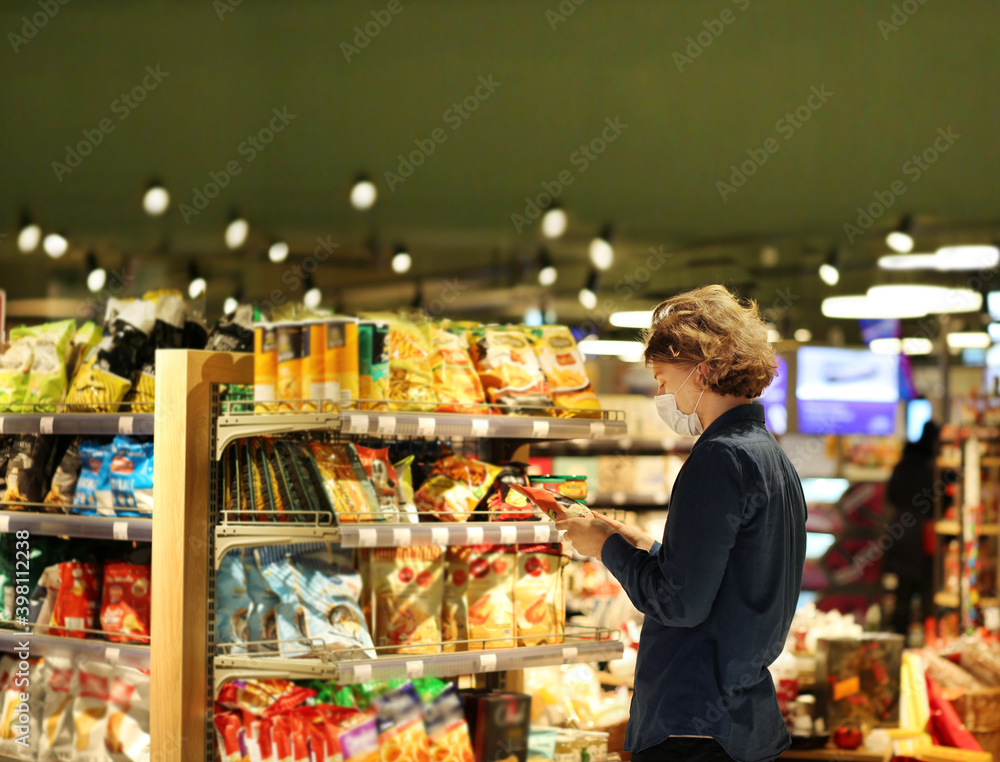Supermarket shopping, face mask and gloves,Young man shopping in supermarket, reading product information.