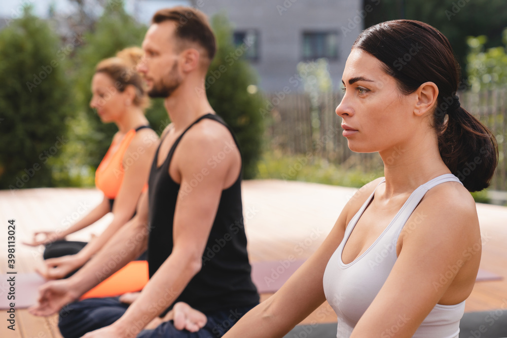 Side view shot of beautiful adults meditating in lotus during yoga classes outside