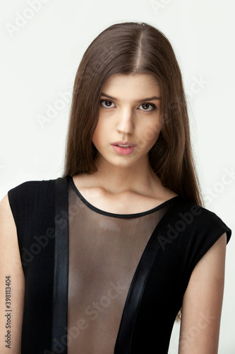 Close up of a brunette girl with seductive look and natural make up, long hair, dressed in black, over white background.