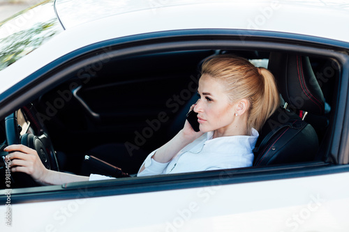 Beautiful blonde woman on the road talking on the phone behind the wheel of a white car © dmitriisimakov