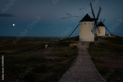Exterior view of windmills in the landscape in spring at dusk with full moon in the Alcazar de San Juan, Ciudad Real, Spain