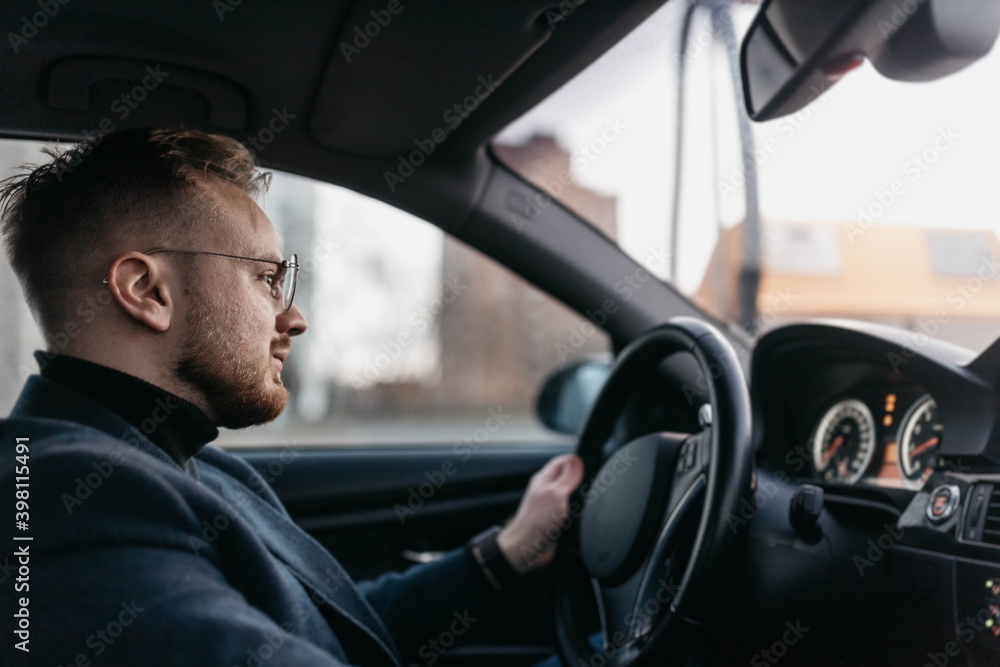 male driver in business clothes and glasses drives a car in winter.