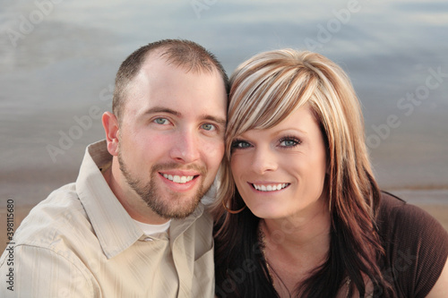 Canvas Print happy young healthy couple sitting on beach with heads touching
