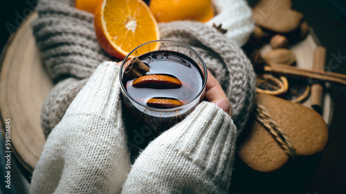 warm drinks in cold weather, a glass of gluntwine in women's hands, on the table oranges, cookies, spices and a warm scarf