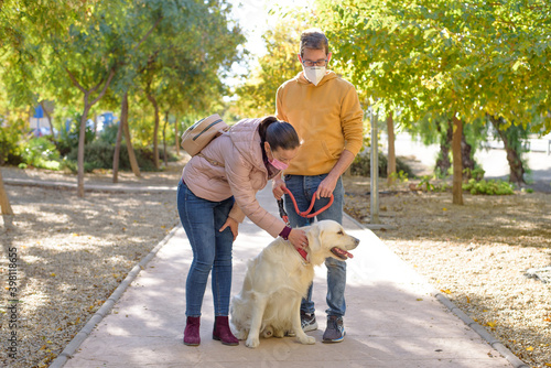 Young white couple in medical surgical masks holding walks with dog in the summer forest. family, europe, hugs, coronavirus, illness, infection, quarantine, virus, pet domestic isolation