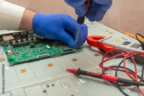 Repair of LCD TV in service center. Hands of engineer remove monitor parts with screwdriver and test it with multimeter. Selective focus