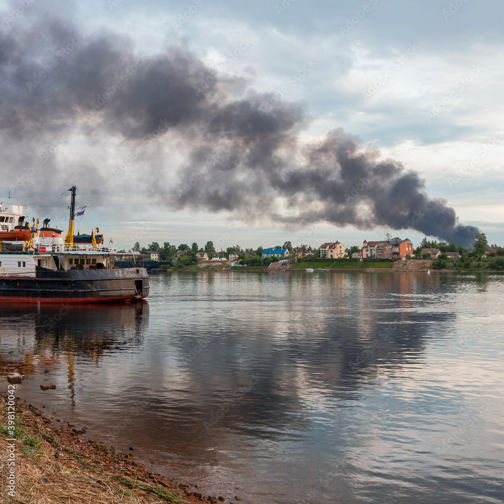view of the Neva River with a cargo ship at the pier and a dangerous cloud of black smoke from a burning building. Fire and disaster concept