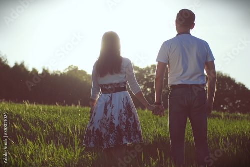 zakochani kobieta i mężczyzna spacerując , trzymając się za ręce po łące w wysokiej trawie podczas zachodu słońca z nadzieją i wiarą wypatrują się w zachód słońca