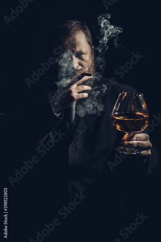 Solid confident bearded man in suit with glass of whisky and cigar with fume
