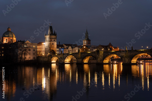  illuminated stone Charles Bridge and the flowing river Vltava and lights from street lighting in the center of Prague in the Czech Republic at night