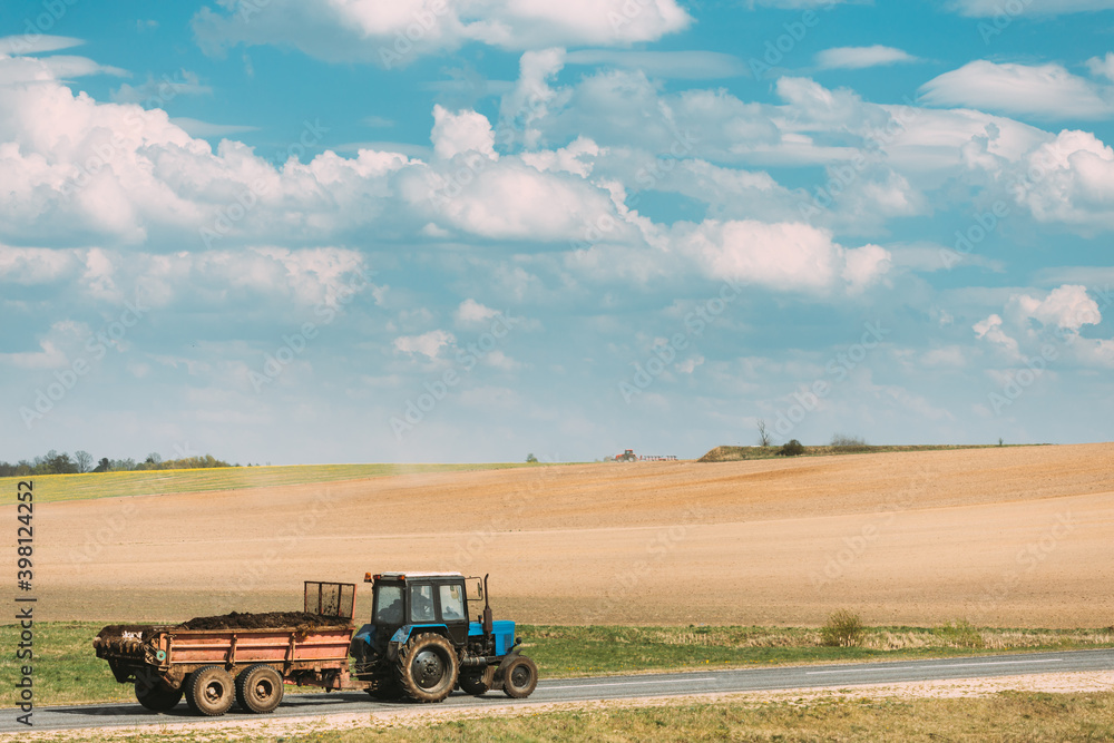 Fototapeta premium Tractor With Cart And Compost Moving On Country Road In Summer Season. Agricultural Landscape