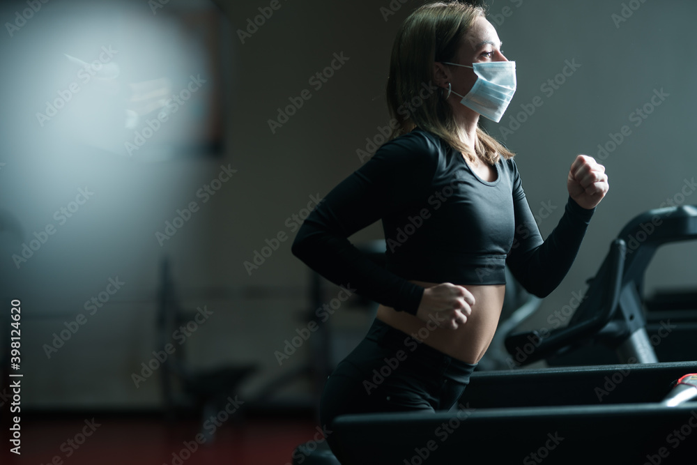 A fitness trainer girl in a medical mask is engaged on a treadmill, develops the lungs during a coronavirus pandemic