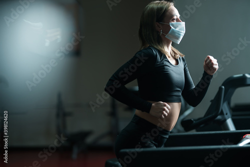 A fitness trainer girl in a medical mask is engaged on a treadmill, develops the lungs during a coronavirus pandemic
