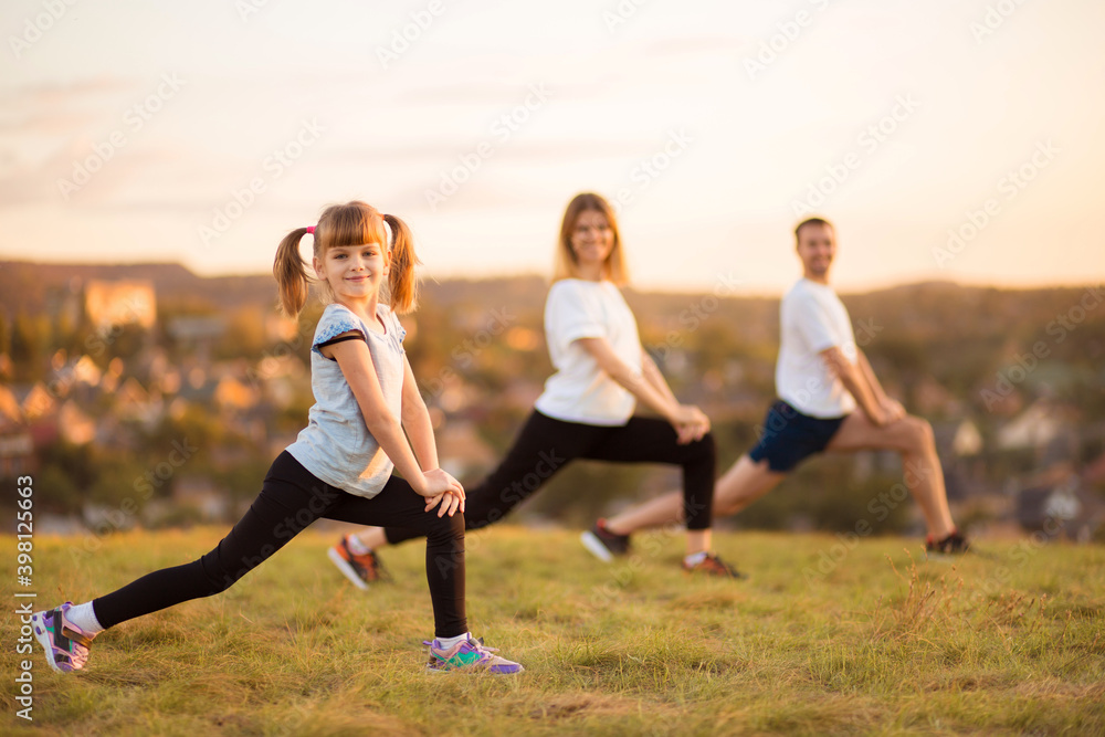 Parents instill sports habits in their child by example, focus on child. Happy sporty family doing stretching exercises, practices yoga outdoor. Mom dad and daughter doing sport exercises Parents instill sports habits in their child by example, focus on child. Happy sporty family doing stretching exercises, practices yoga outdoor. Mom dad and daughter doing sport exercises