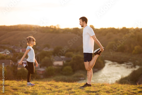 Father and cute daughter doing yoga outside in bright sunny day, lovely emotions. together at park. Family stretching after sport. Healthy habits