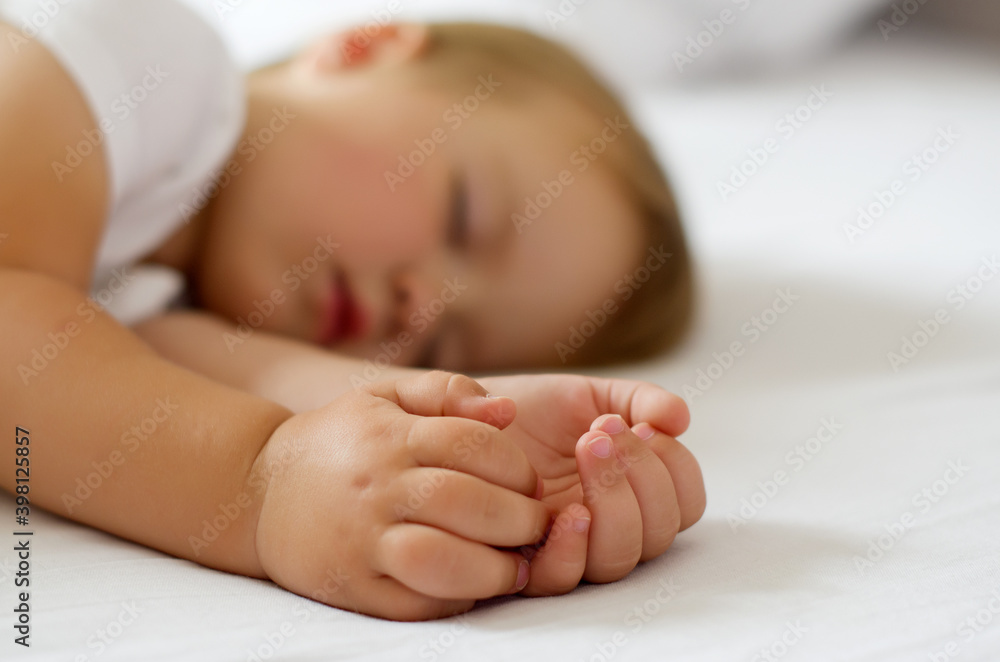 Blonde child baby toddler sleeping in white bed. Selective focus. Close-up macro shot. Focus on foreground. The touching and lovely moment. Blonde child baby toddler sleeping in white bed. Selective focus. Close-up macro shot. Focus on foreground. The touching and lovely moment.