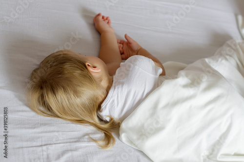 Faceless toddler girl with blonde hair sleeping on white bed. Rear view of a two year old child girl sleeping a beautiful and comfortable bed