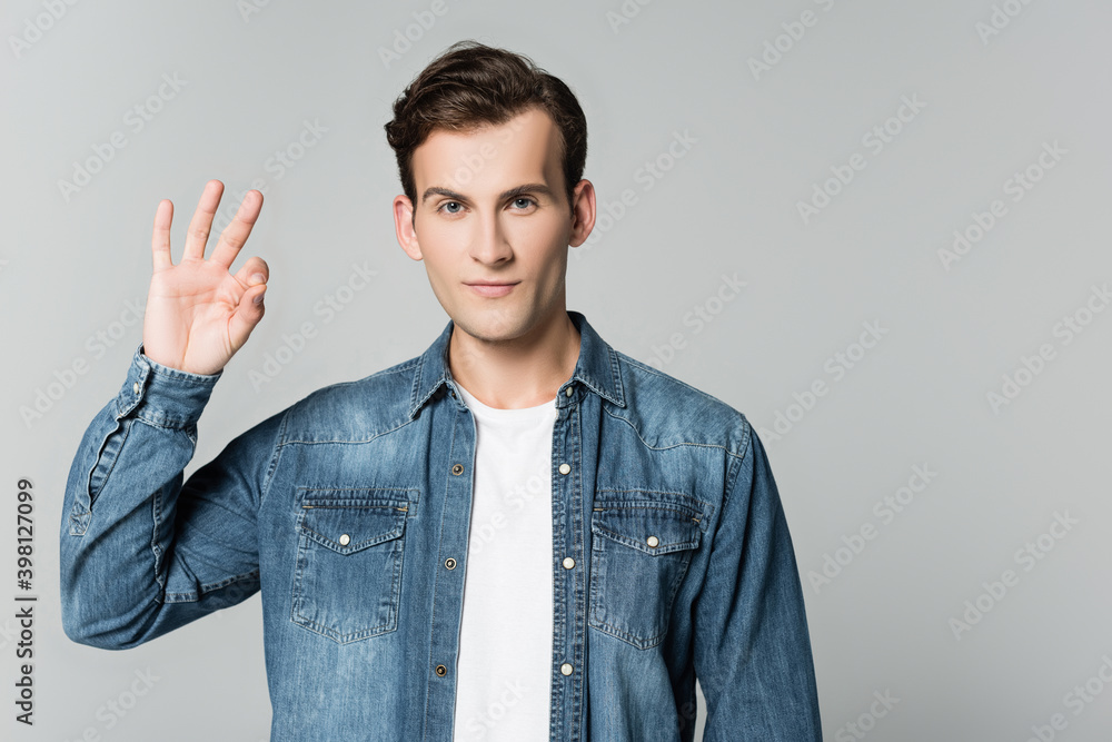 Brunette man in denim jacket showing ok gesture isolated on grey Brunette man in denim jacket showing ok gesture isolated on grey