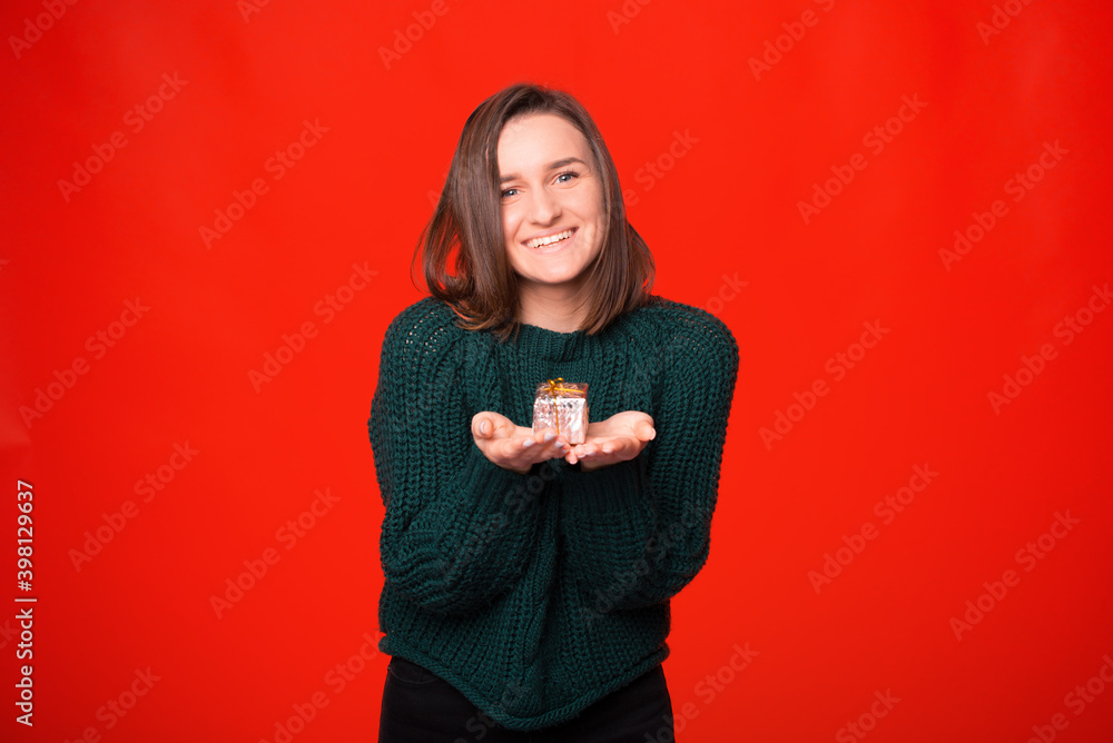 Young pretty smiling girl is holding a small gift box over red background. Young pretty smiling girl is holding a small gift box over red background.