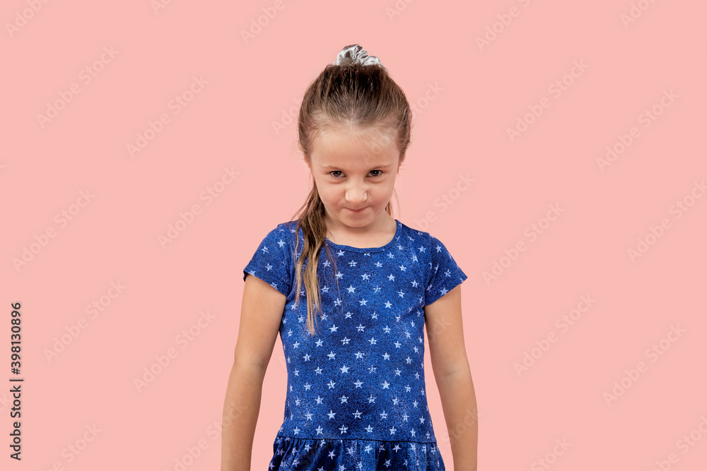 An angry girl looks from under her forehead at the camera. Blue dress with a small star. Pink isolated background. An angry girl looks from under her forehead at the camera. Blue dress with a small star. Pink isolated background.