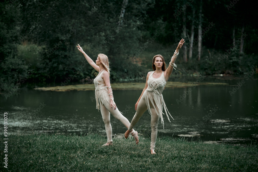 Young women in beige dresses with macrame dancing in nature. There is a large lake behind. The concept of natural cosmetics and harmony with nature. My hair is blowing in the wind. Young women in beige dresses with macrame dancing in nature. There is a large lake behind. The concept of natural cosmetics and harmony with nature. My hair is blowing in the wind.