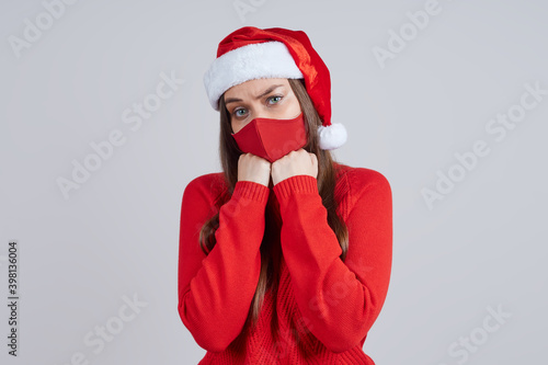 Sad woman in a protective mask  in a Santa hat  hands at the chin. Concept of christmas  new year quarantined.