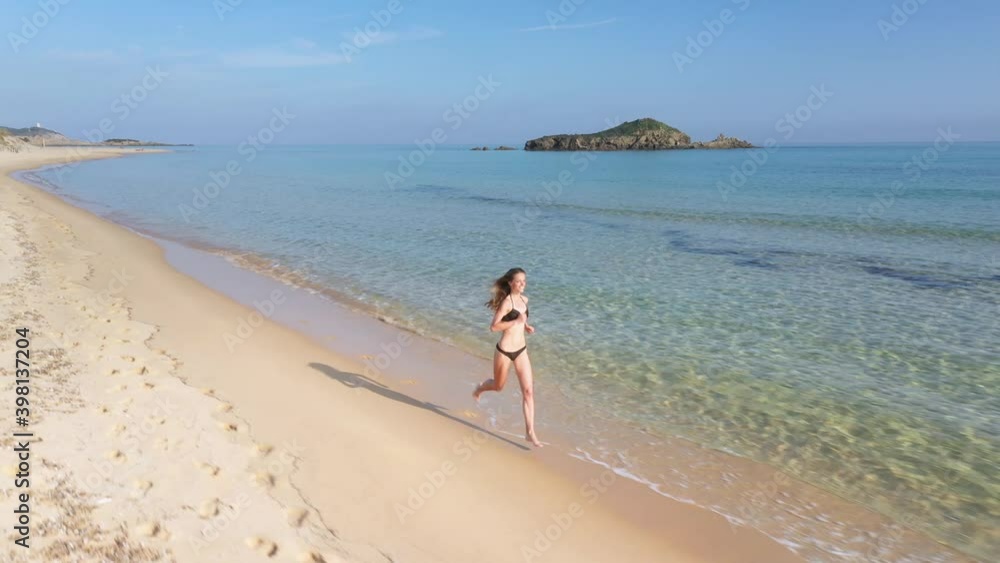 Aerial of a beautiful woman walking down a beautiful white sand beach on Sardinia, Italy Aerial of a beautiful woman walking down a beautiful white sand beach on Sardinia, Italy