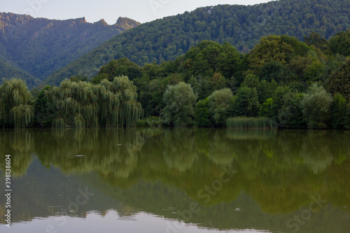 Beautiful summer landscape in the mountains: mountain lake, mountain slopes in green trees, reflection of mountains and trees in the lake water