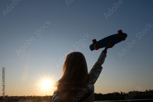 Silhouette of the woman with pennyboard in her raised hand photo