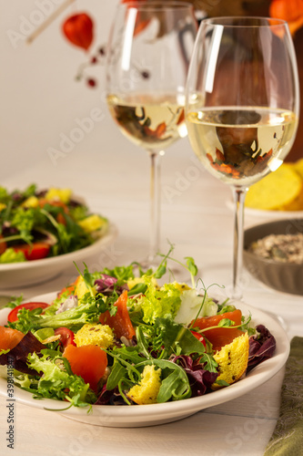 Light breakfast or dinner  mix salad with salmon and different seeds and two glasses of white wine  plate with salad and cornbread close up