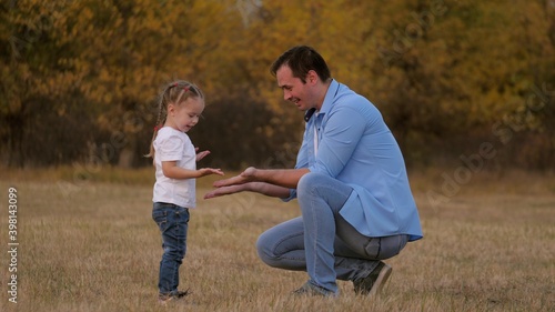 Dad and little daughter say hello. The child claps his father on the palm, a happy family plays in the park. Teamwork of baby and daddy. A fun outdoor game, dad loves his baby. Healthy family