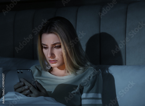 Young woman using smartphone in bed at night. Nomophobia and sleeping disorder problem © New Africa