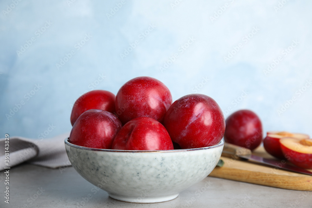 Delicious ripe plums in bowl on grey table Delicious ripe plums in bowl on grey table