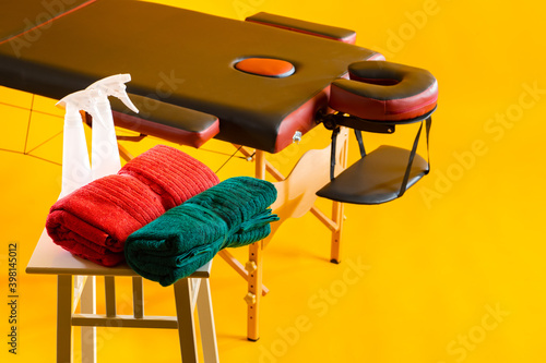 Place for massage therapy. SPA treatment table. Massage table on a yellow background. Towels and pulverizers next to massage table. Concept - services of a massage therapist. Place for SPA treatments