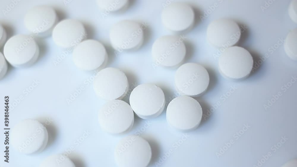 Small white round pills fly into the frame. On a white background, close-up, contains people, real time, medicine, health Small white round pills fly into the frame. On a white background, close-up, contains people, real time, medicine, health