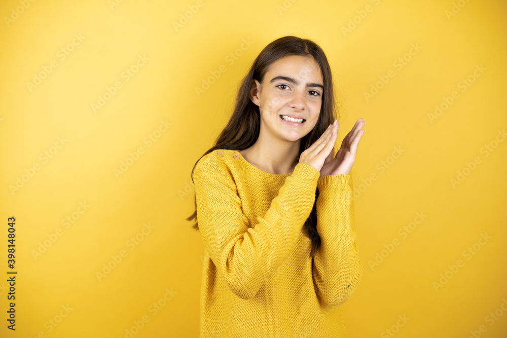 Pretty girl wearing a yellow sweater standing over isolated yellow background clapping and applauding happy and joyful, smiling proud hands together Pretty girl wearing a yellow sweater standing over isolated yellow background clapping and applauding happy and joyful, smiling proud hands together