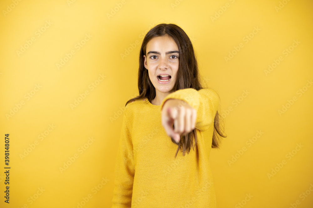 Pretty girl wearing a yellow sweater standing over isolated yellow background pointing with finger surprised ahead, open mouth amazed expression, something on the front Pretty girl wearing a yellow sweater standing over isolated yellow background pointing with finger surprised ahead, open mouth amazed expression, something on the front